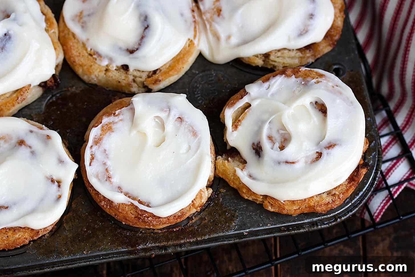 Freshly baked cinnamon roll biscuits cooling in a muffin tin, ready to be frosted.