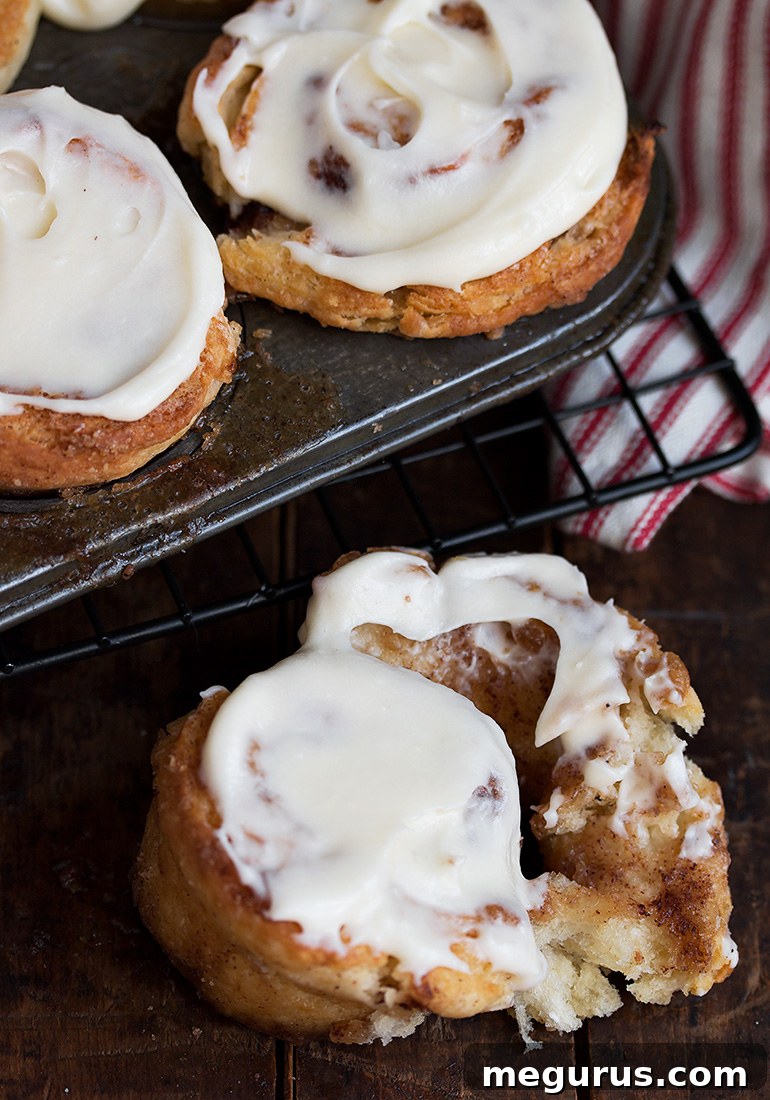 Close-up of a stack of fluffy cinnamon roll biscuits topped with melted cream cheese frosting.
