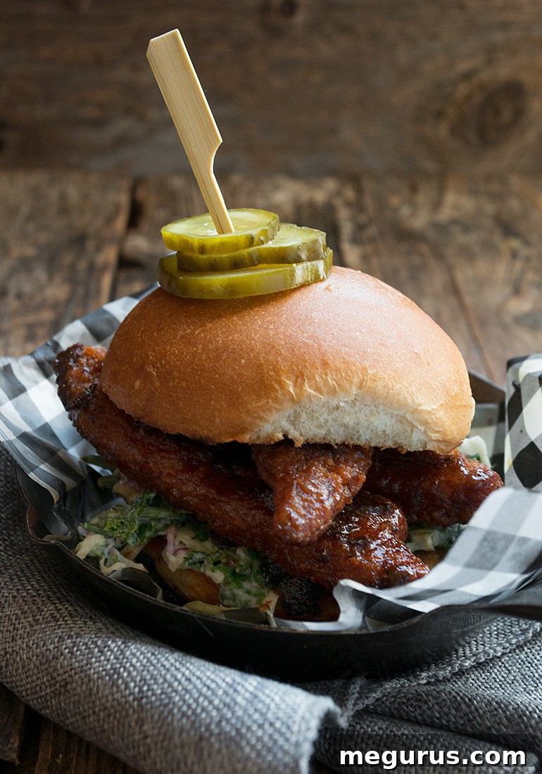 Close-up of a Nashville Hot Chicken Strip Burger showing crispy chicken, coleslaw, and pickles