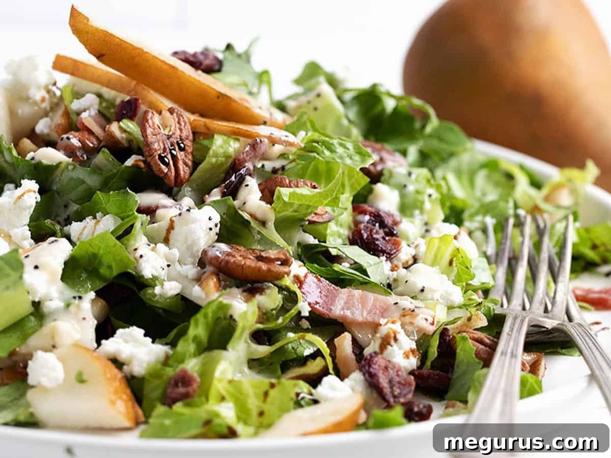 A vibrant Fall pear chopped salad on a white plate, with whole pears subtly blurred in the background, hinting at the fresh, seasonal ingredients.