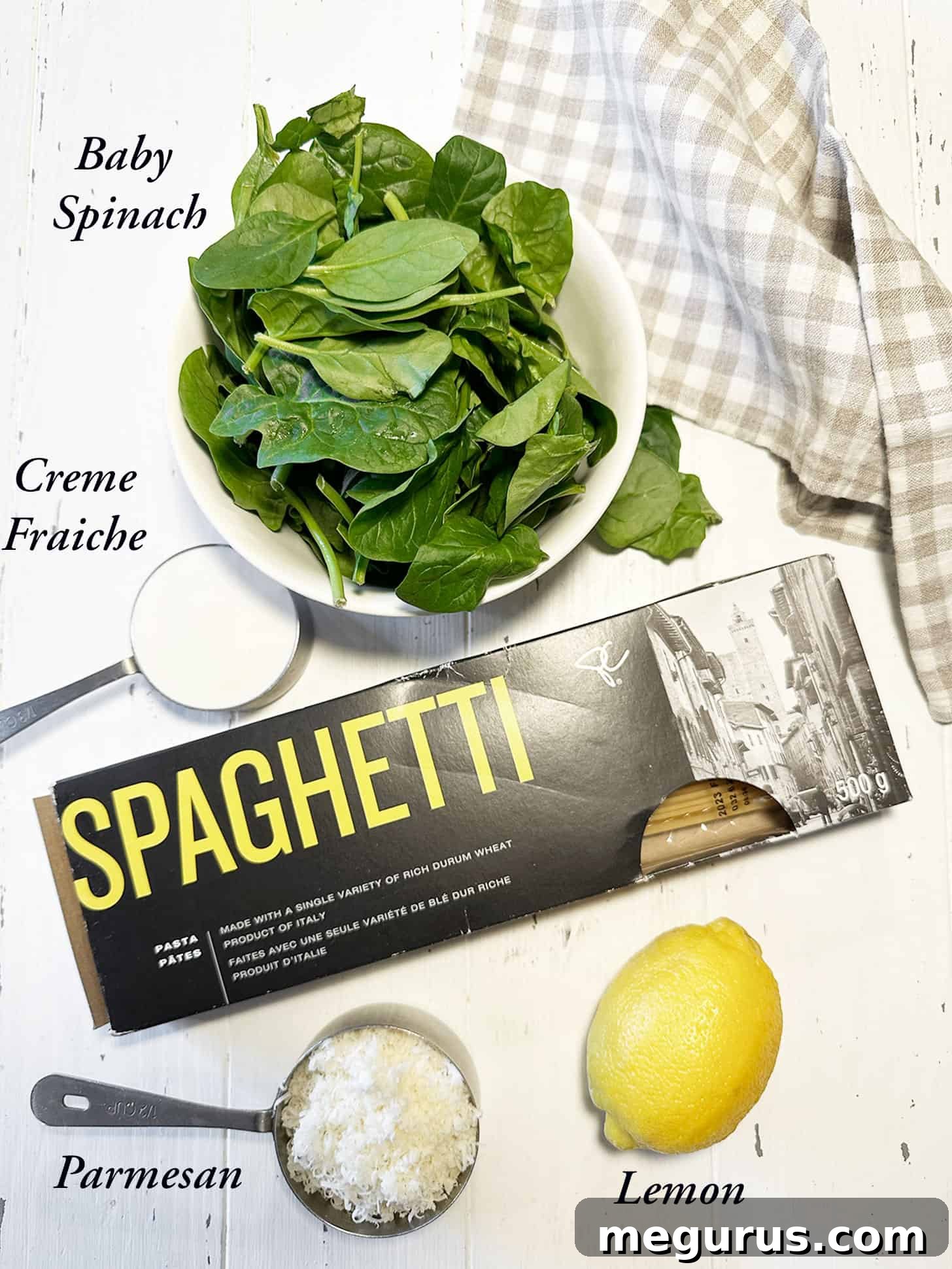 Assorted ingredients laid out for making lemon spinach pasta, including pasta, spinach, lemons, and cheese.
