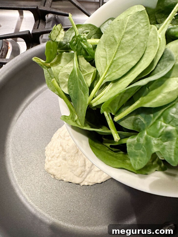 Fresh baby spinach being added to the skillet containing the sauce.