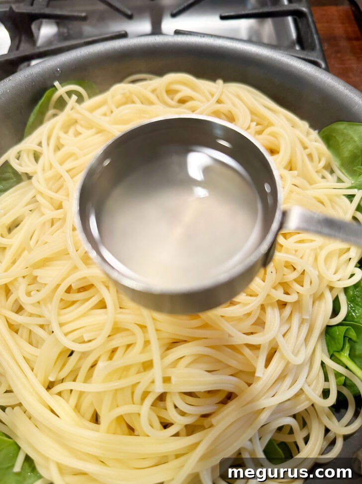 Hot pasta being transferred from the pot to the skillet with sauce and spinach using tongs.