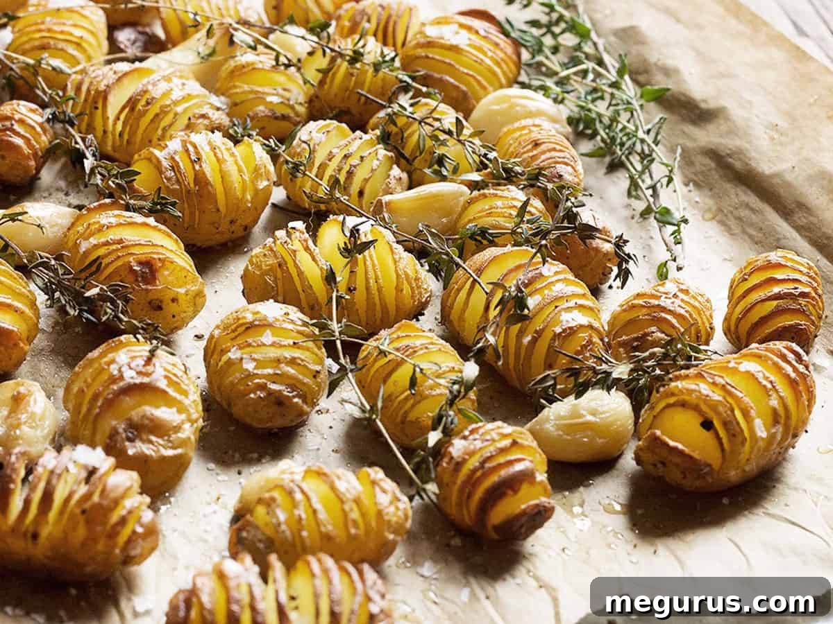 Golden-brown Hasselback mini potatoes roasted on parchment paper, garnished with fresh herbs.