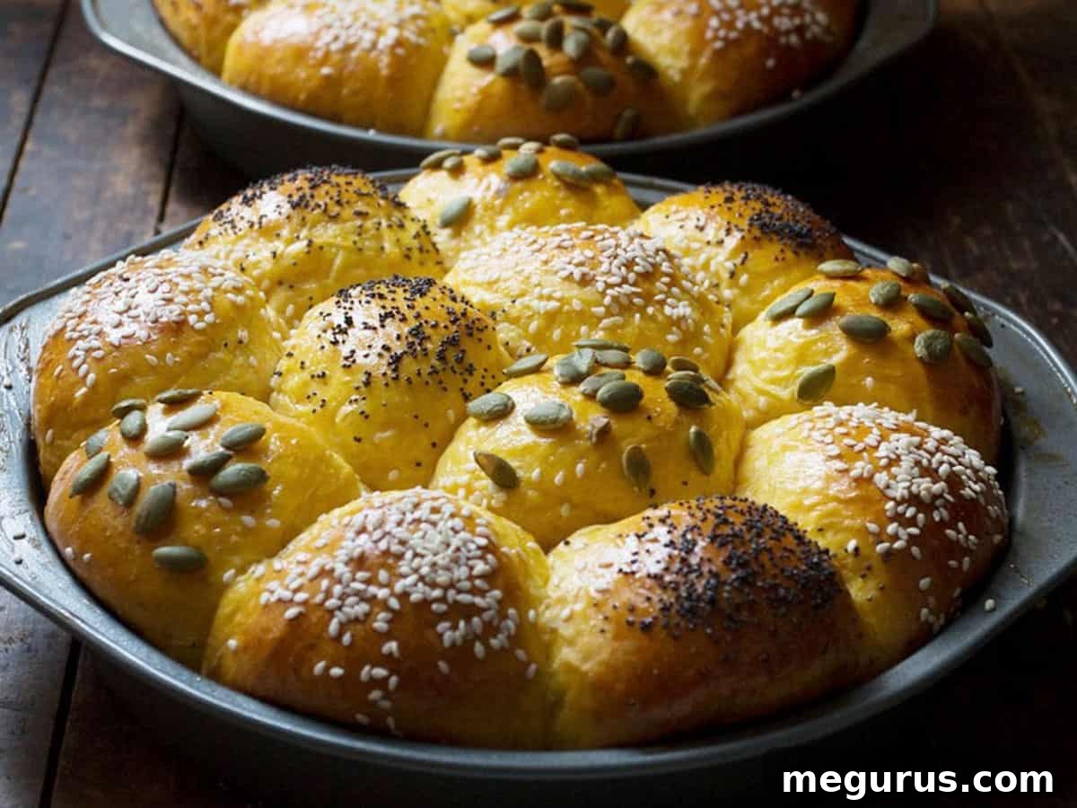 Freshly baked honey pumpkin rolls in baking pans, golden brown and topped with an assortment of seeds.