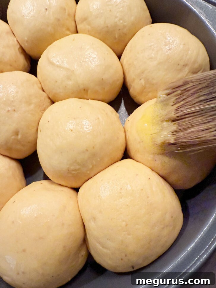 Brushing the tops of the proofed rolls with an egg wash before baking.