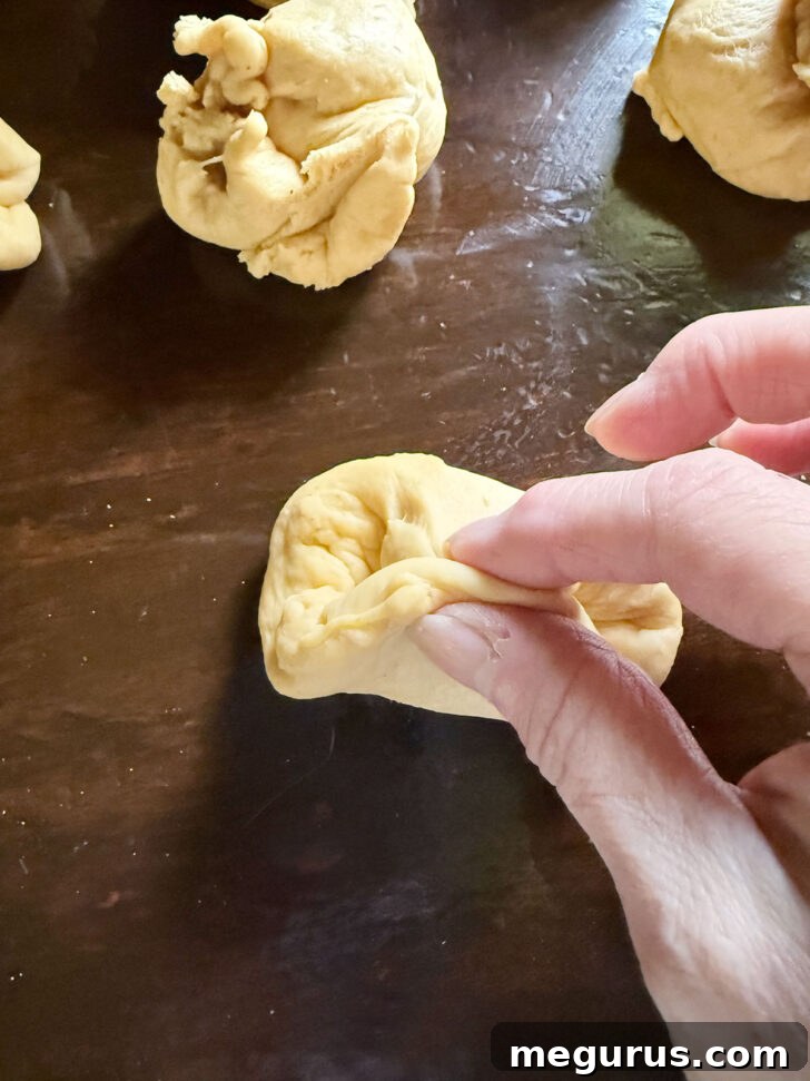 Pinching the underside of the dough balls to create a smooth surface.