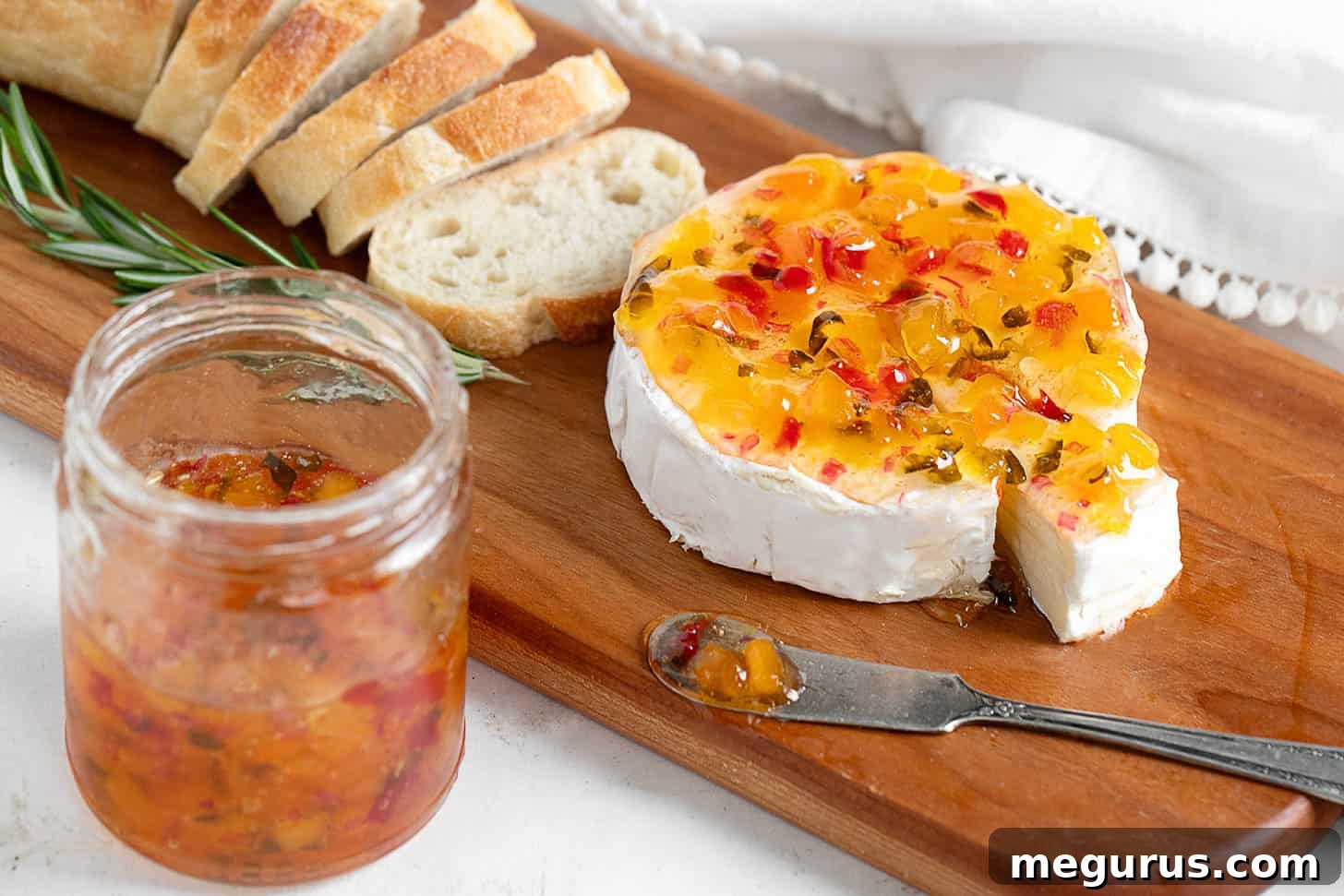 Apricot jalapeño jelly generously spooned over a wheel of Brie cheese, served with crusty bread on a rustic wooden board.