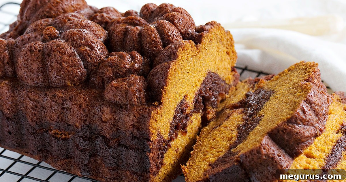 A perfectly sliced pumpkin chocolate swirl bread on a cooling rack, showcasing its beautiful, distinct chocolate and pumpkin layers.