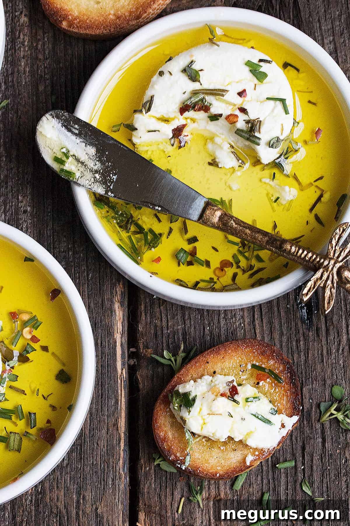 Two small white bowls of marinated goat cheese, garnished with fresh herbs, ready to serve.