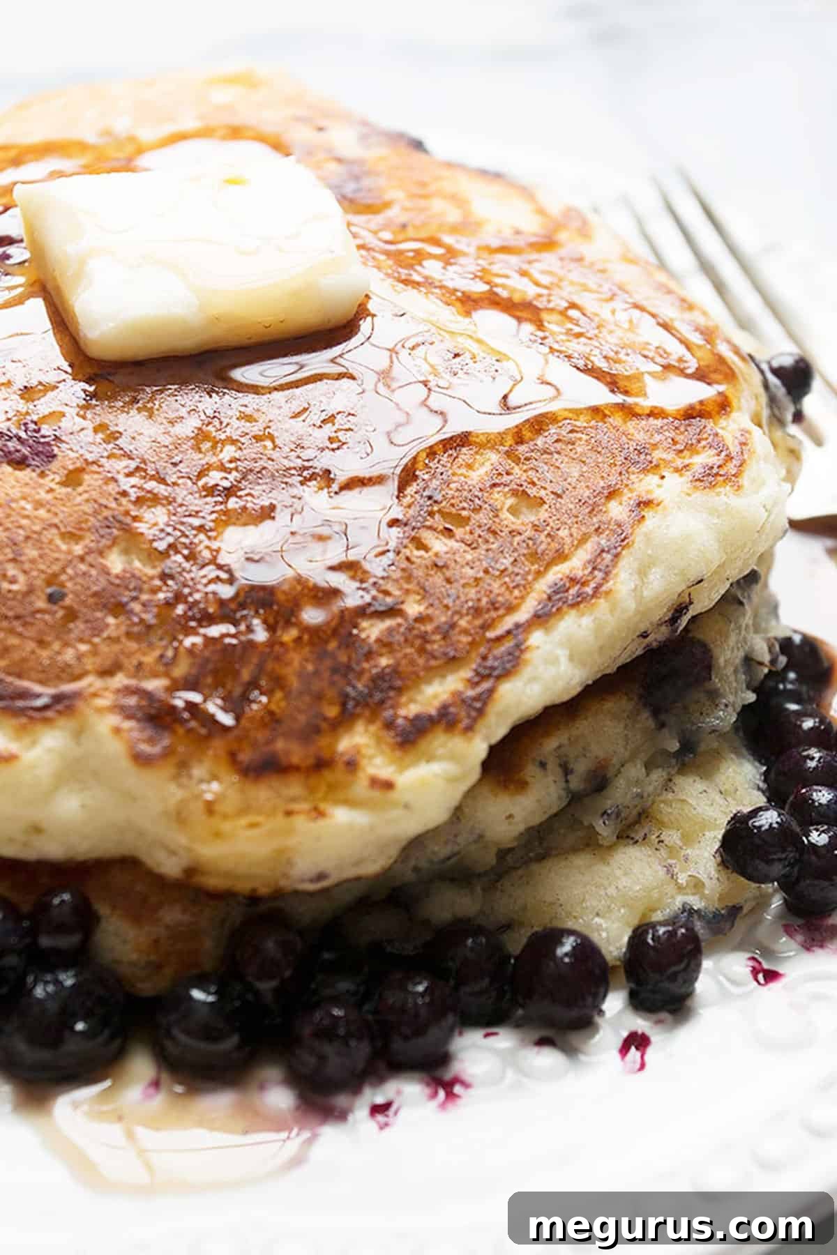 Close-up of a stack of golden buttermilk blueberry pancakes, with melted butter and fresh blueberries on top.