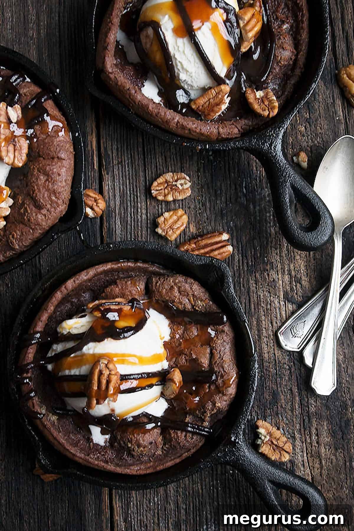 Two mini chocolate Dutch babies, one topped with ice cream and sauces, in cast iron skillets