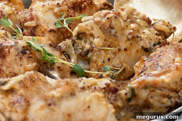 Chicken Dijon in baking dish with spoon, glistening with sauce.