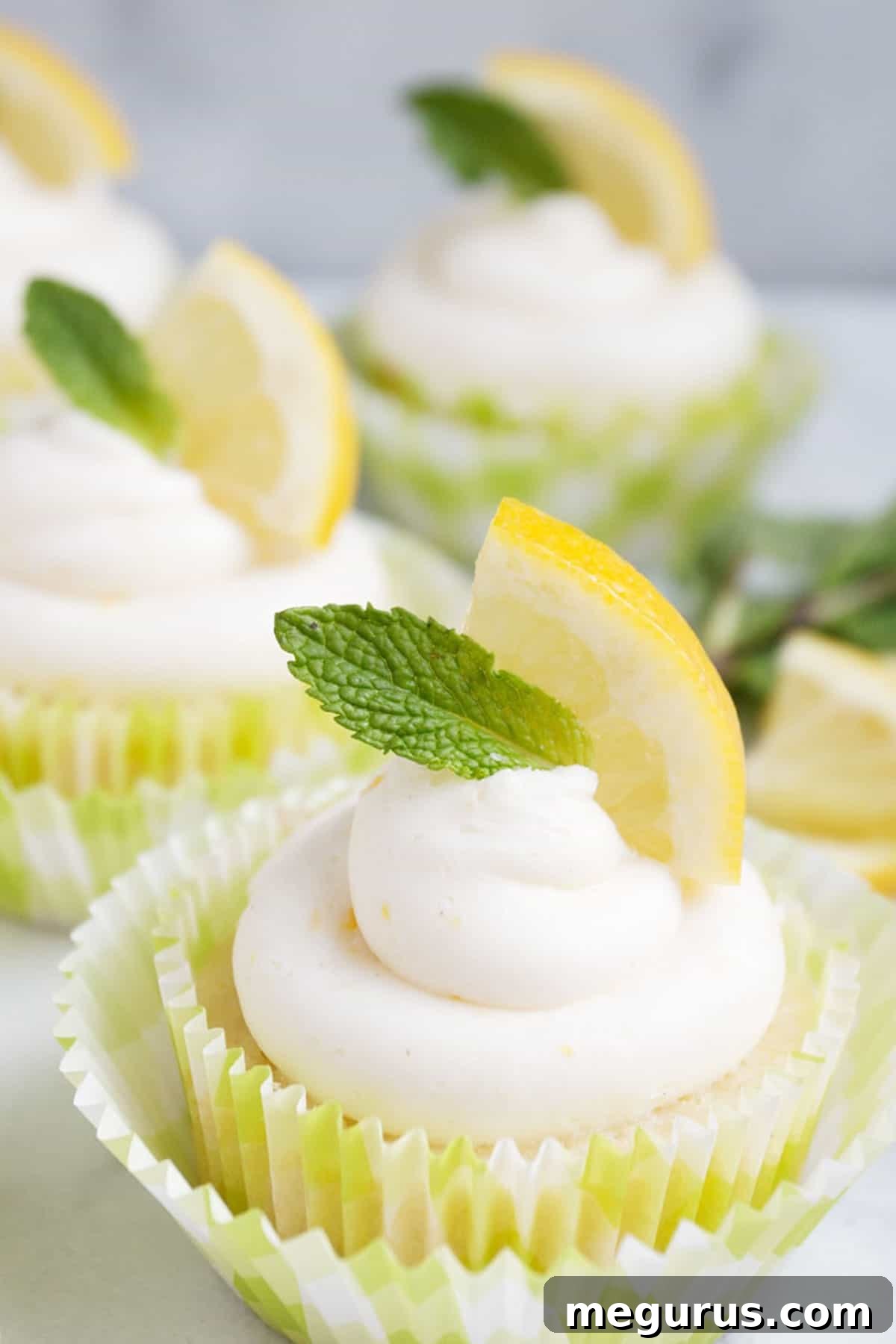 Close-up of a single lemon cupcake with lemon slice and mint sprig on top, showing fluffy frosting