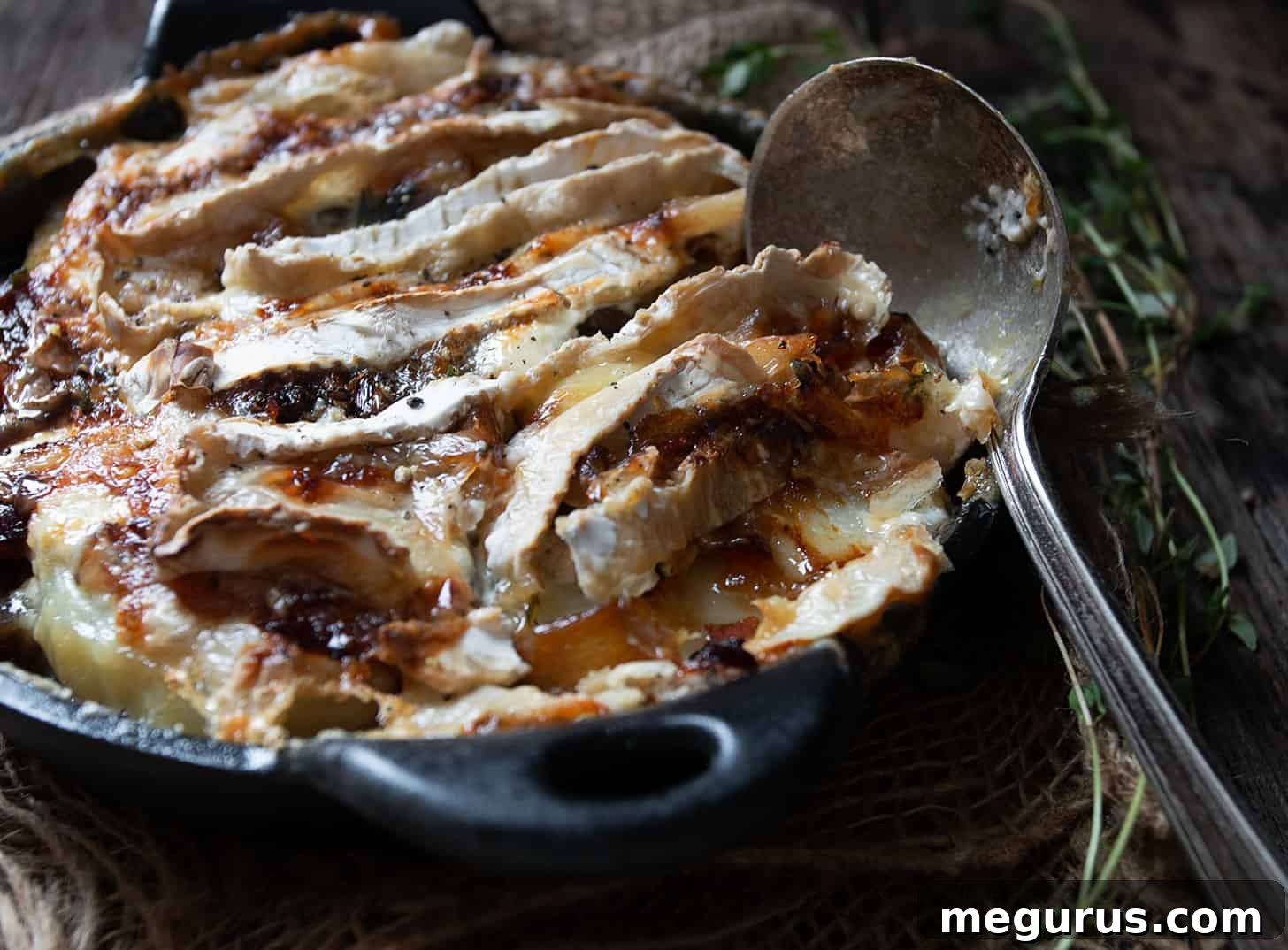 Golden brown Tartiflette in a small cast iron skillet, ready to be served, showcasing its cheesy and creamy layers.