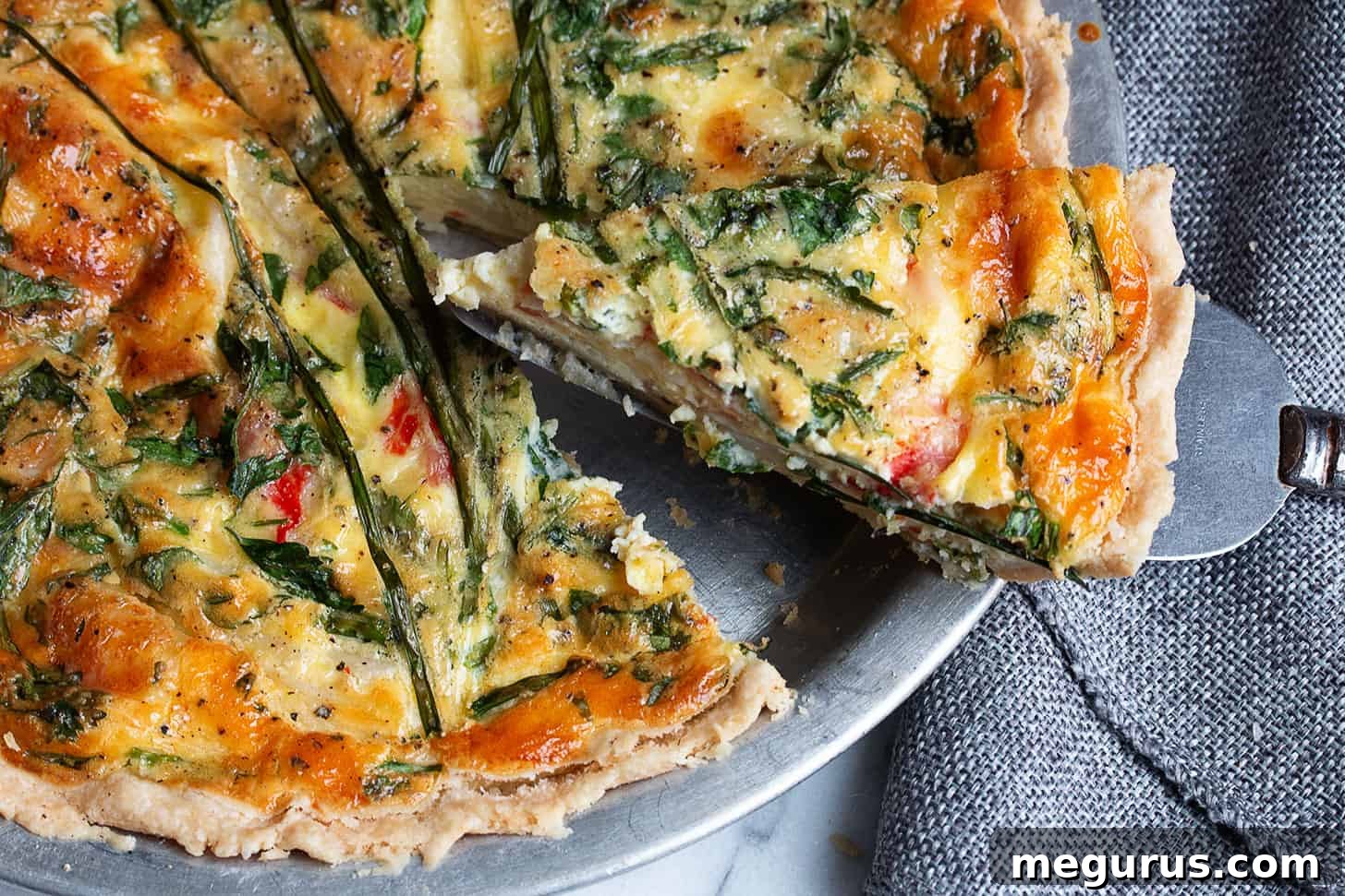 A perfectly sliced crab quiche in a pie dish, showcasing its golden crust and creamy filling