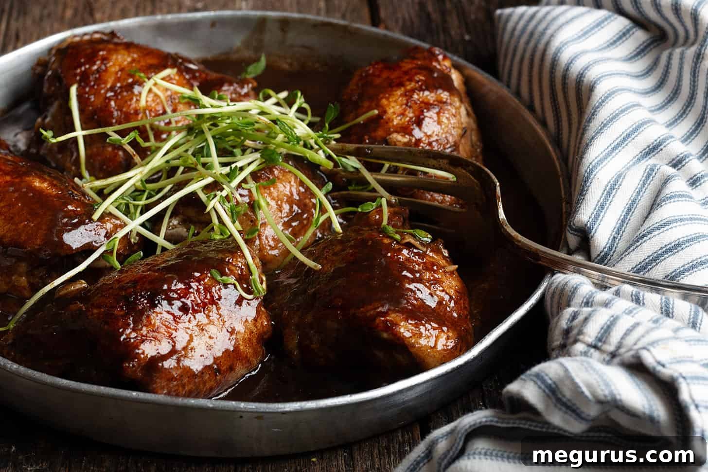 Balsamic chicken thighs in serving dish with fork.