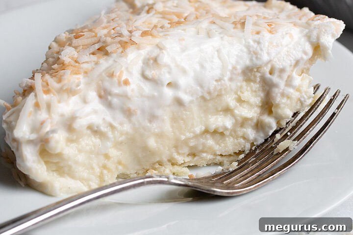 A mouthwatering slice of homemade coconut cream pie on a plate with a fork, showing off its thick, creamy filling, flaky crust, and decadent toppings.
