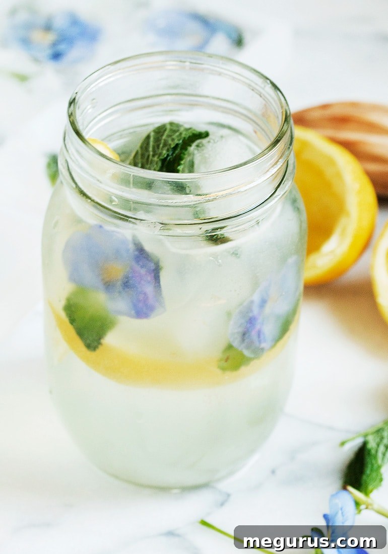 A refreshing Homemade Lemonade Sparkler drink, garnished with lemon slices and mint sprigs, highlighting the beautiful pansy ice cubes.