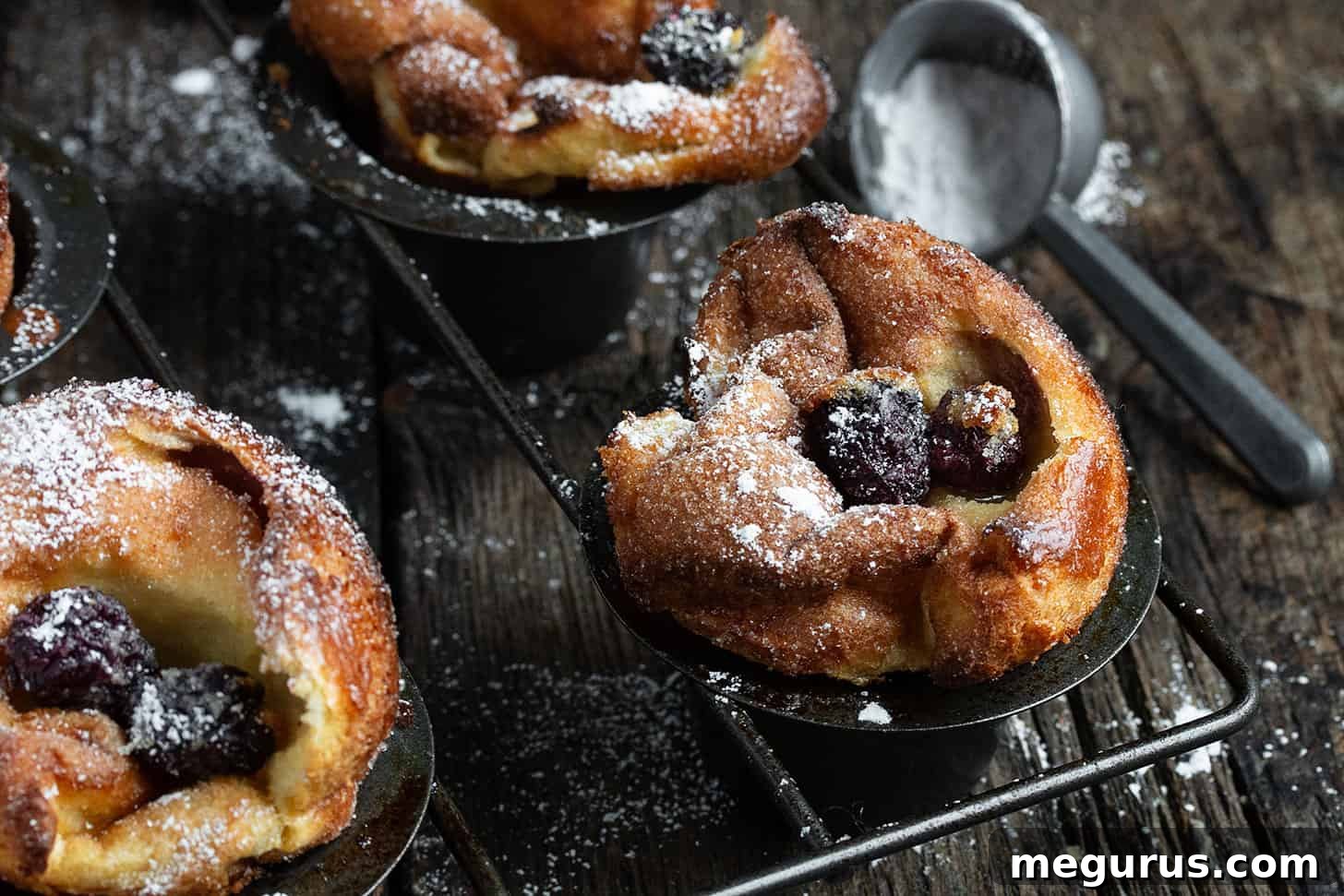 Freshly baked sugar crusted blackberry popovers in a popover pan, showcasing their impressive rise and golden crust.