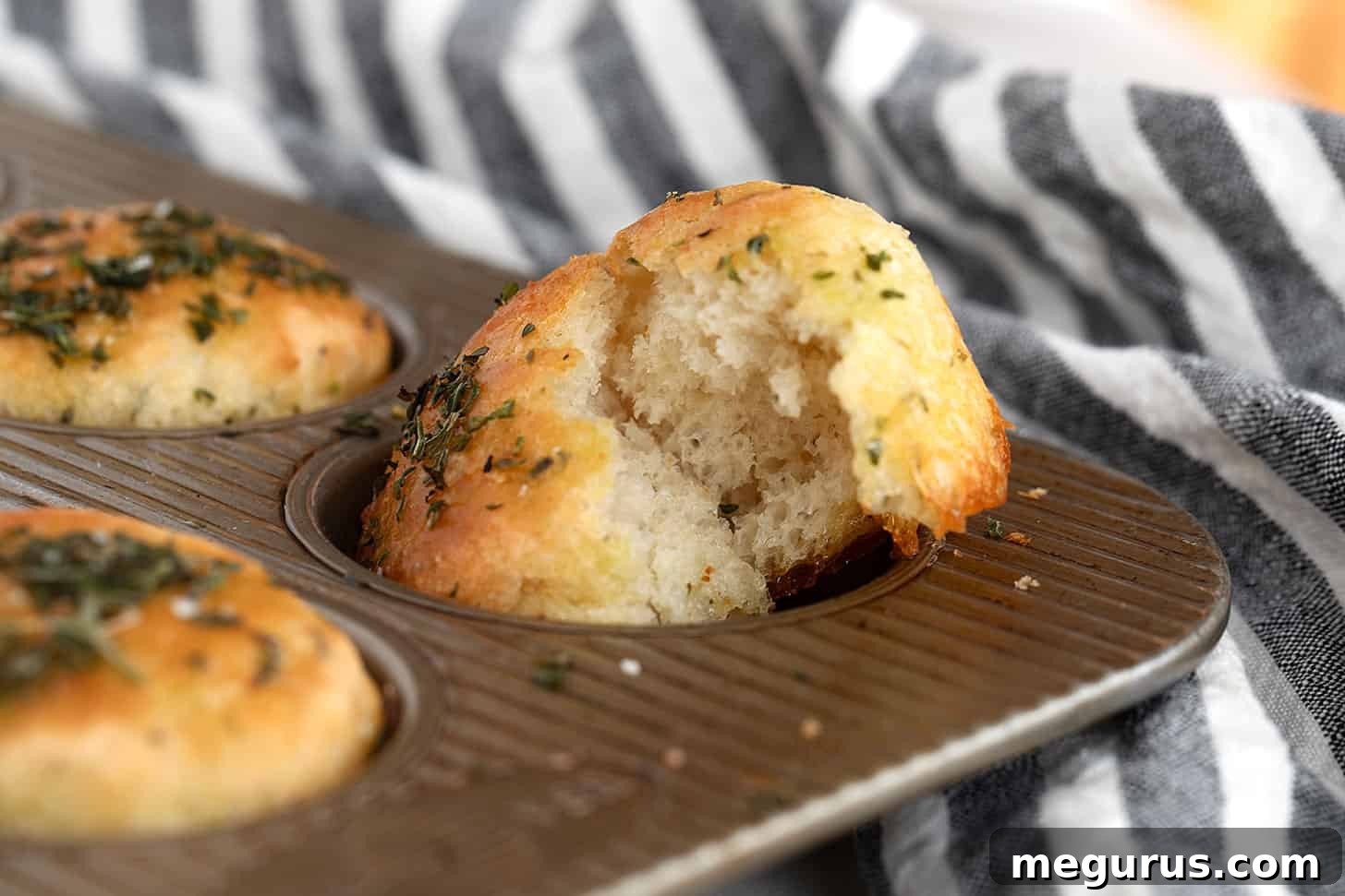 Golden brown herb focaccia muffins freshly baked in a muffin tin.