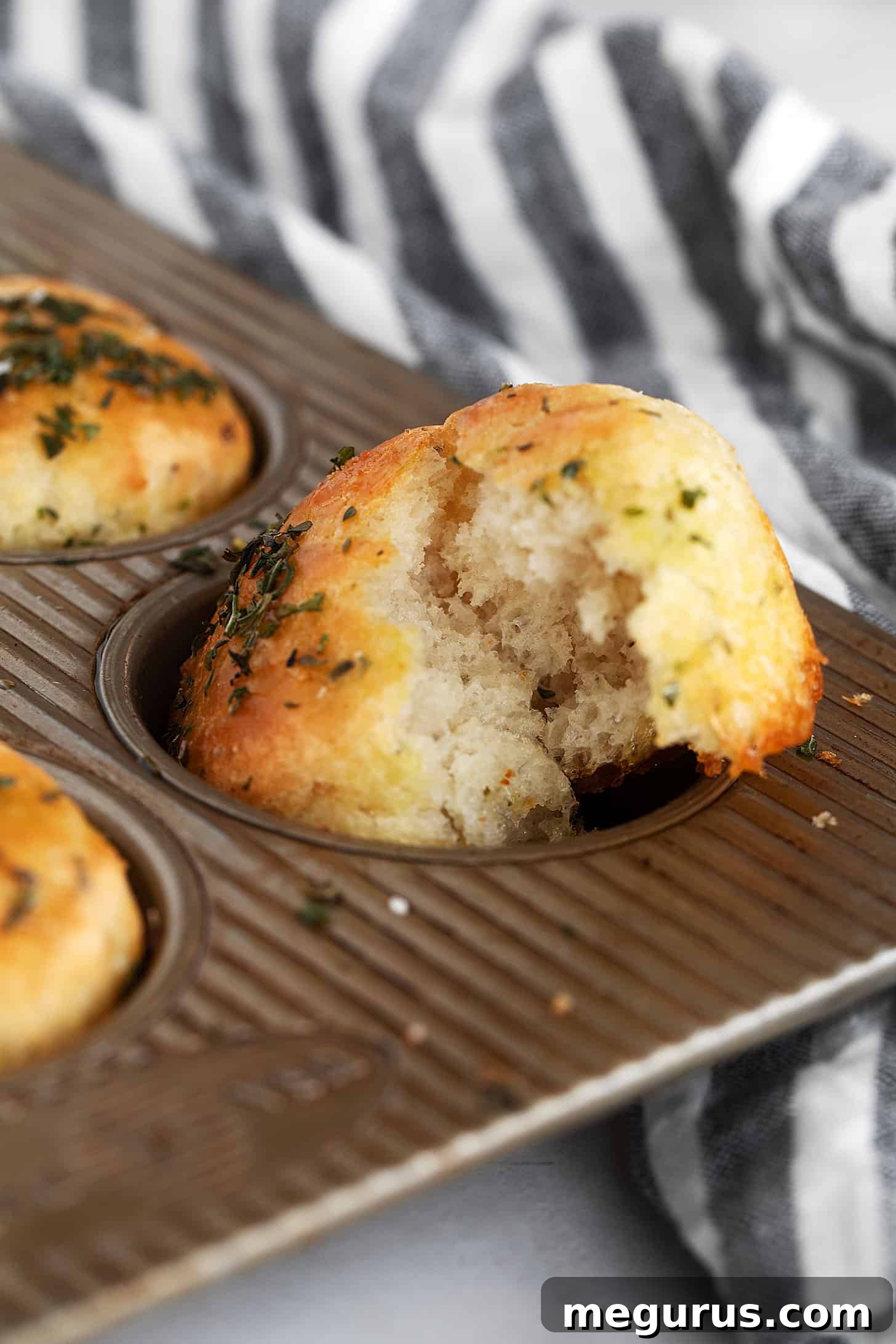 Close-up of herb focaccia muffins in muffin cups, showing their golden crust.