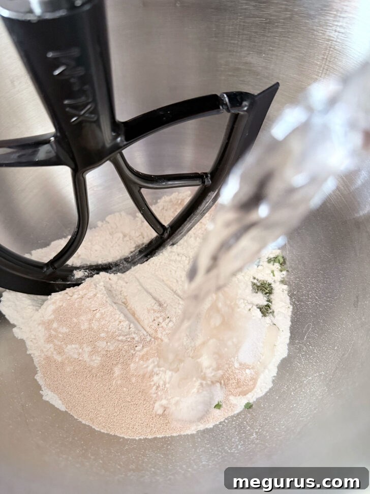 Lukewarm water being added to the mixer bowl with dry ingredients.