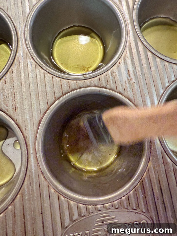 A pastry brush spreading olive oil up the sides of muffin cups.