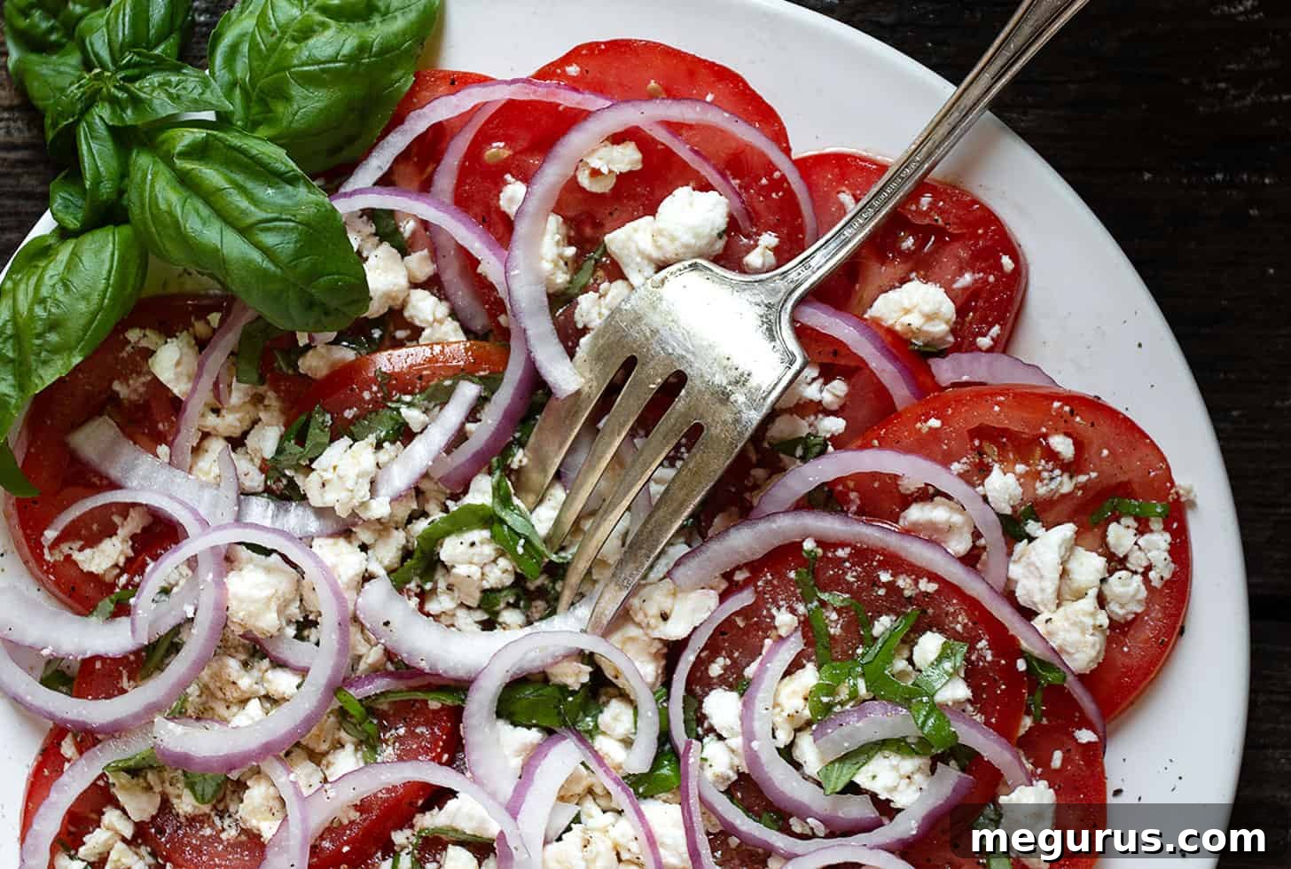 Vibrant tomato feta salad on a white plate, showcasing ripe tomatoes, red onions, and crumbled feta