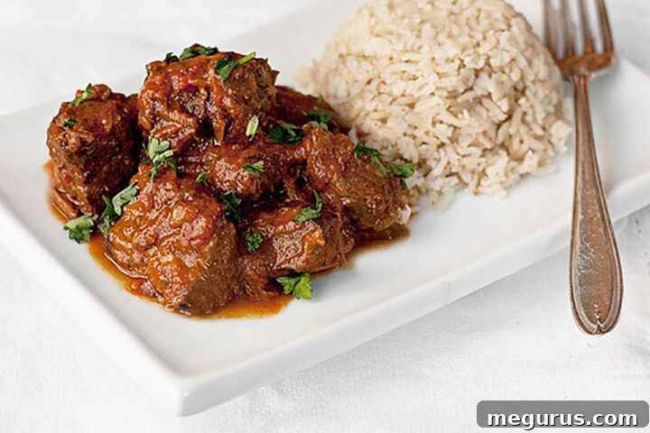 A serving of spiced beef curry on a white plate with a side of Basmati rice and a fork, ready to eat.