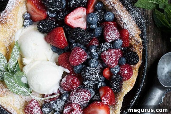 Fresh fruit Dutch Baby pancake in a cast iron skillet with berries and ice cream