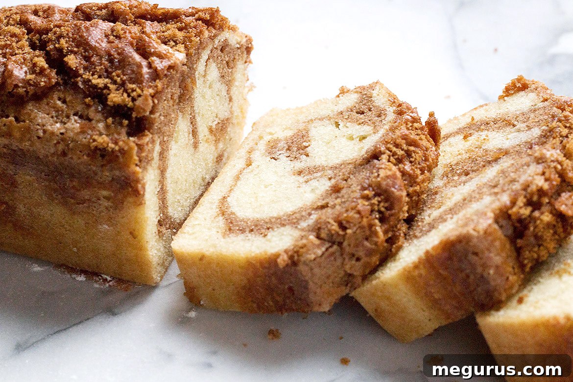 Deliciously sliced cinnamon swirl pound cake loaf on a marble surface, showcasing the beautiful cinnamon ribbon and crunchy topping.
