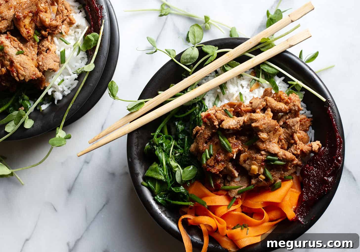 Vibrant spicy pork rice bowl garnished with green onions and chili sauce, ready to be enjoyed with chopsticks