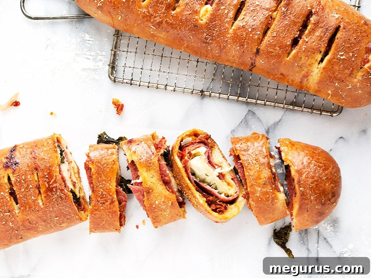 A perfectly baked, golden-brown stromboli, whole and sliced to reveal its delicious layers of meats, cheese, and sun-dried tomato paste.