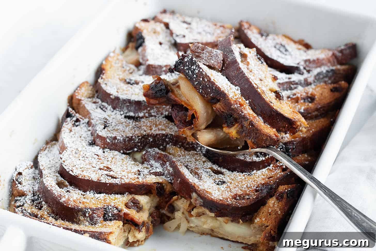 Beautifully baked Gruyere and pear bread pudding in a glass baking dish, with a serving spoon resting beside it.