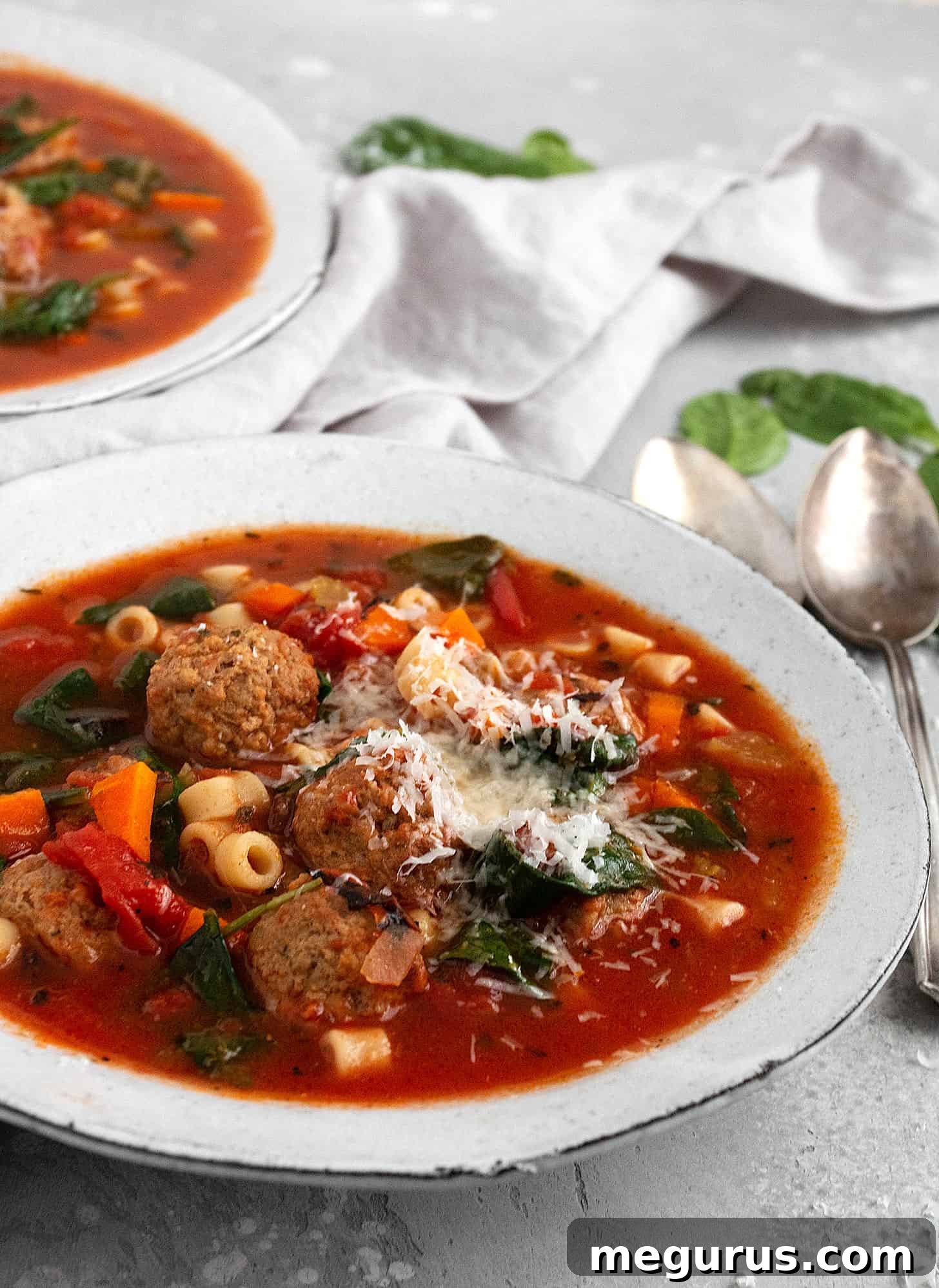 Close-up of a serving of Italian meatball soup in a white bowl, showing the rich broth, small pasta, vibrant vegetables, and meatballs.