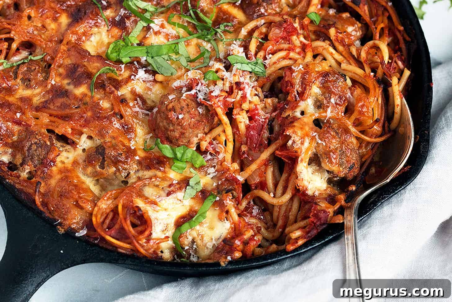 Baked Spaghetti and Meatballs in a cast iron skillet, ready to serve with a spoon