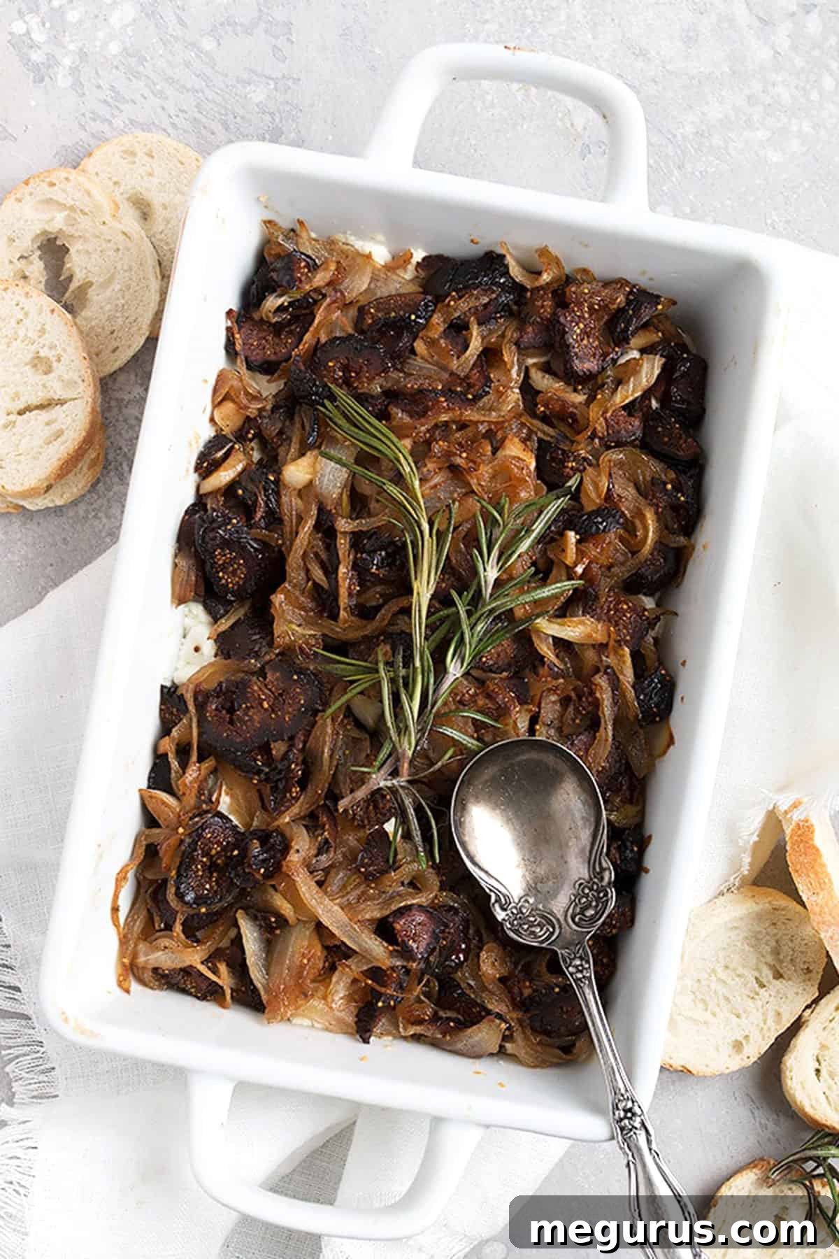Close-up of warm goat cheese fig dip in a white dish, showing the creamy cheese, dark figs, and golden onions