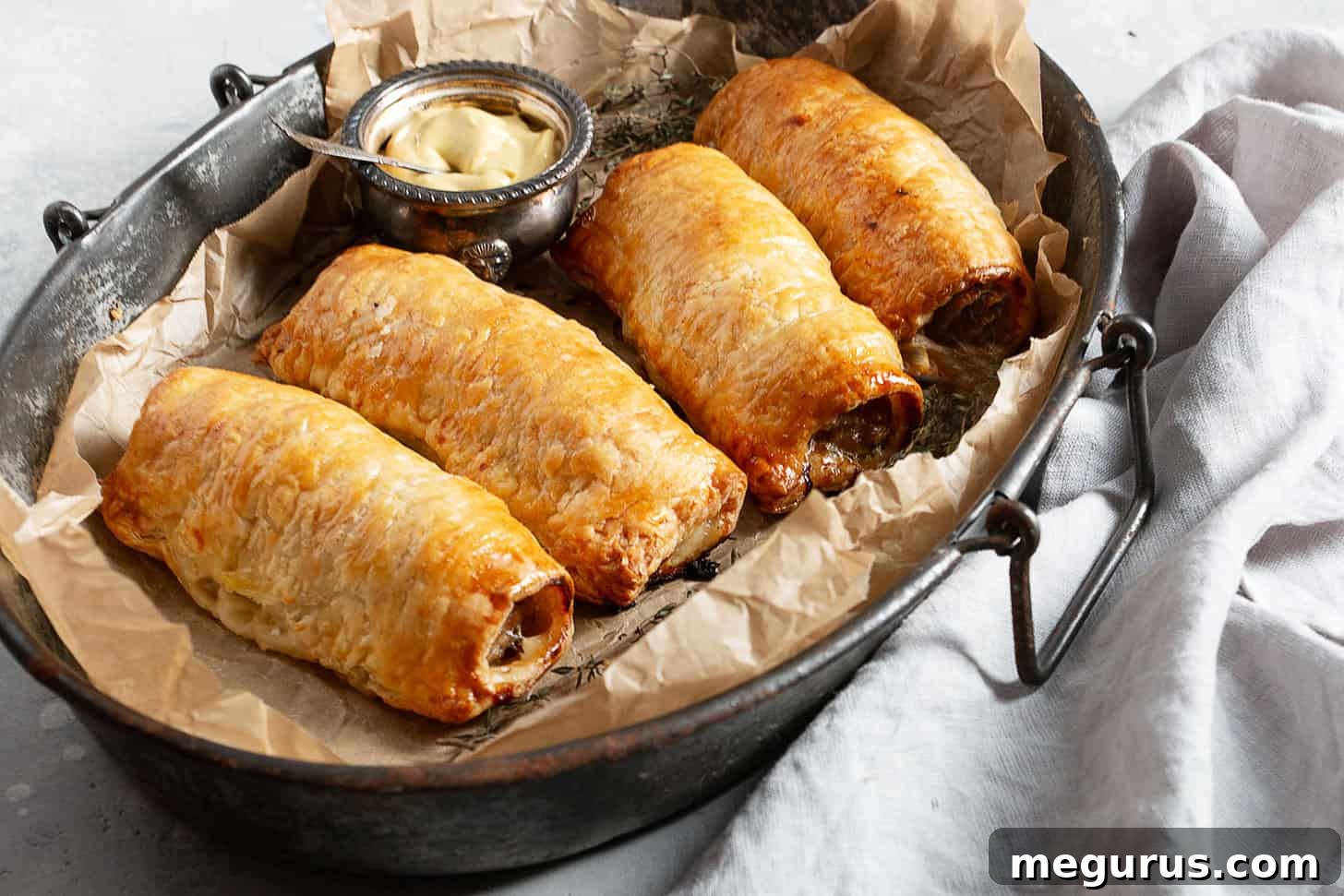Golden brown puff pastry sausage rolls served on a rustic platter, ready to be enjoyed with mustard.