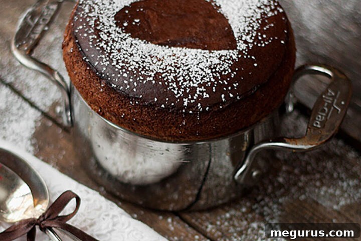 Close-up of a chocolate soufflé perfectly risen in a baking dish, with two spoons ready to serve.