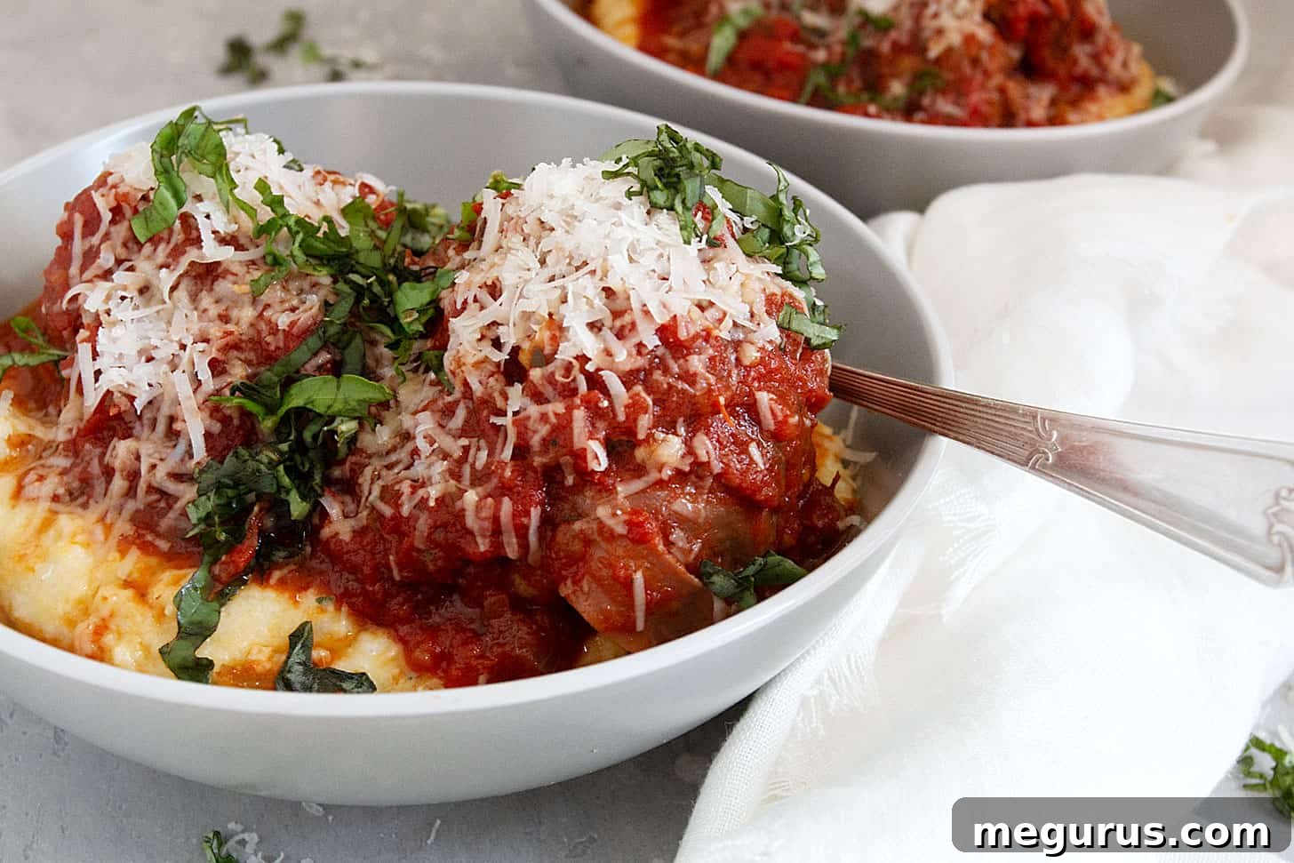 Delicious pork meatballs with prosciutto, served over creamy polenta, garnished with fresh herbs.