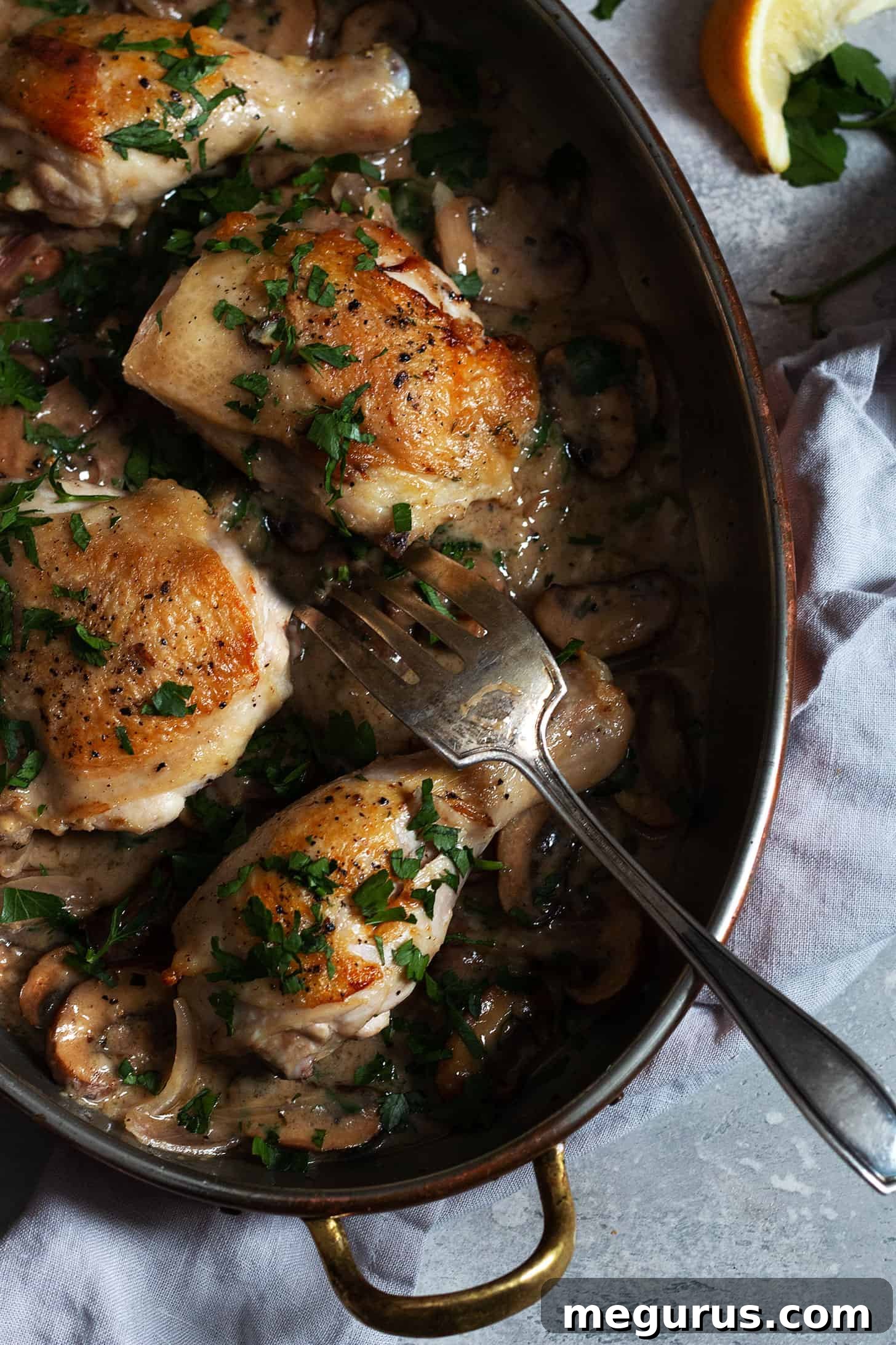 Close-up view of golden Chicken Riesling pieces in a white baking dish, nestled in creamy mushroom sauce with parsley garnish