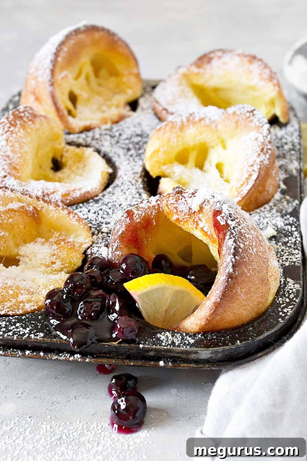 mini Dutch babies in muffin tin with lemons and blueberry sauce