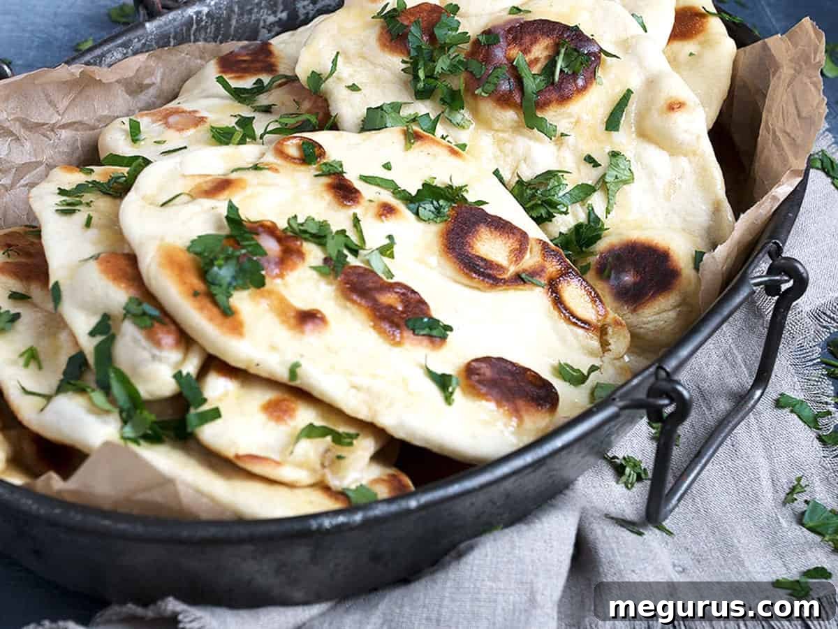 Freshly baked garlic naan bread on a rustic metal platter, garnished with chopped herbs.
