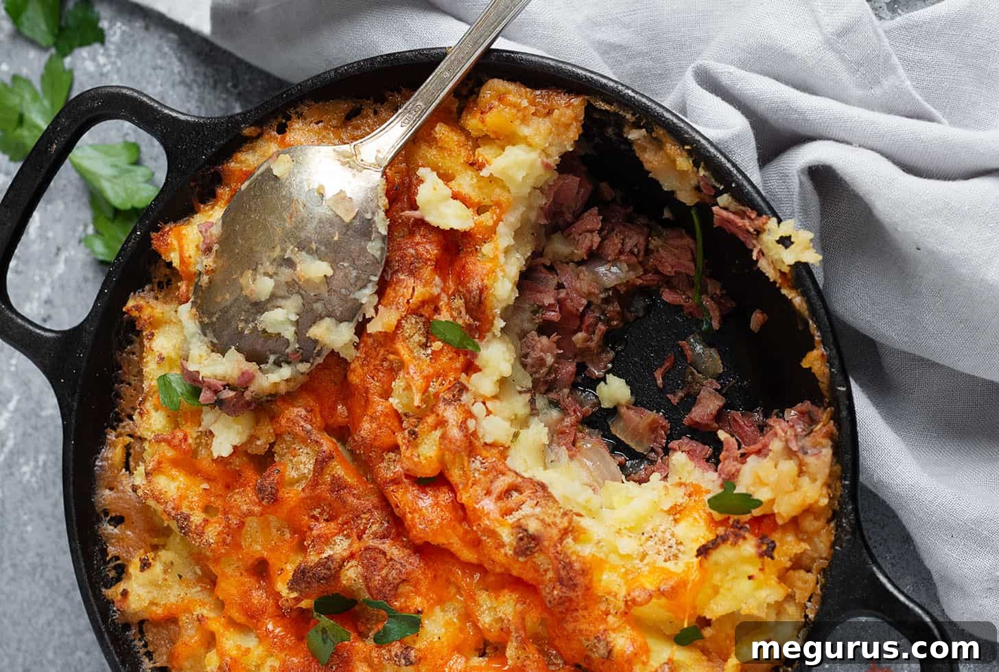 Hearty Corned Beef Cottage Pie, freshly baked in a cast-iron skillet, ready to be served with a large spoon.