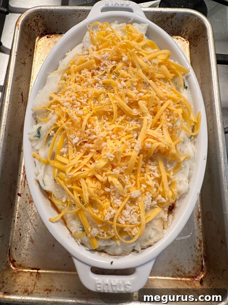 The mashed potato layer beautifully topped with shredded cheddar cheese and a sprinkle of crispy breadcrumbs, ready for baking.