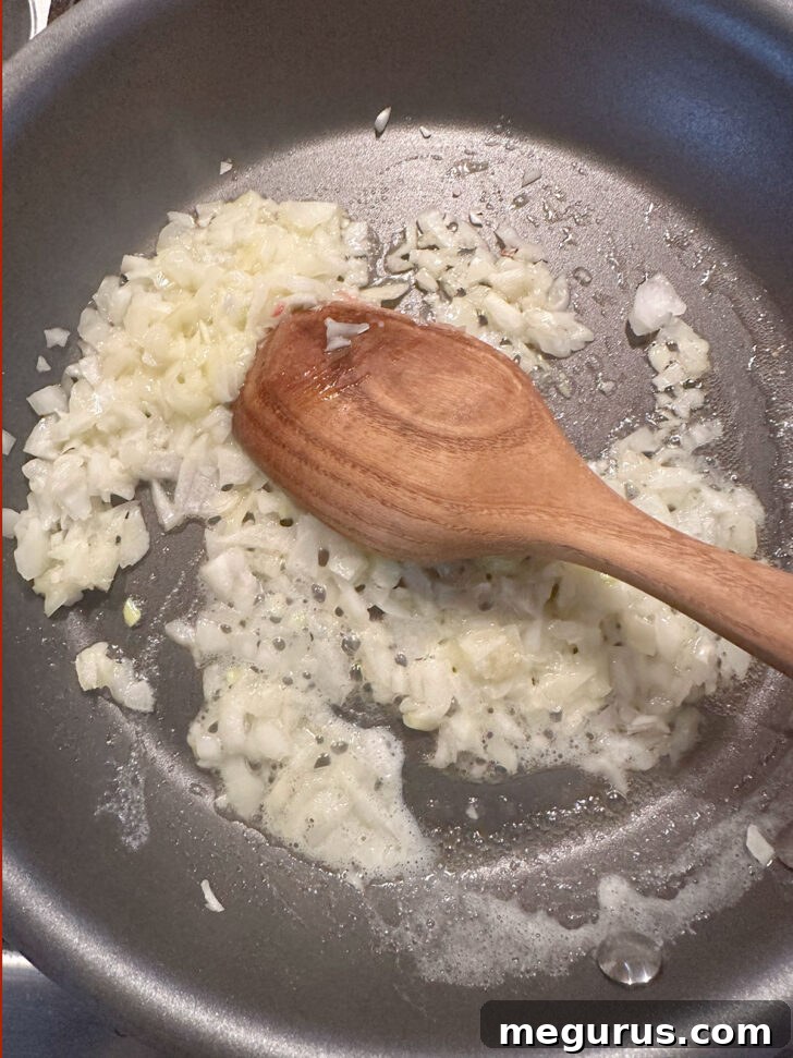 Diced onions gently softening in melted butter in a skillet, turning translucent and fragrant.