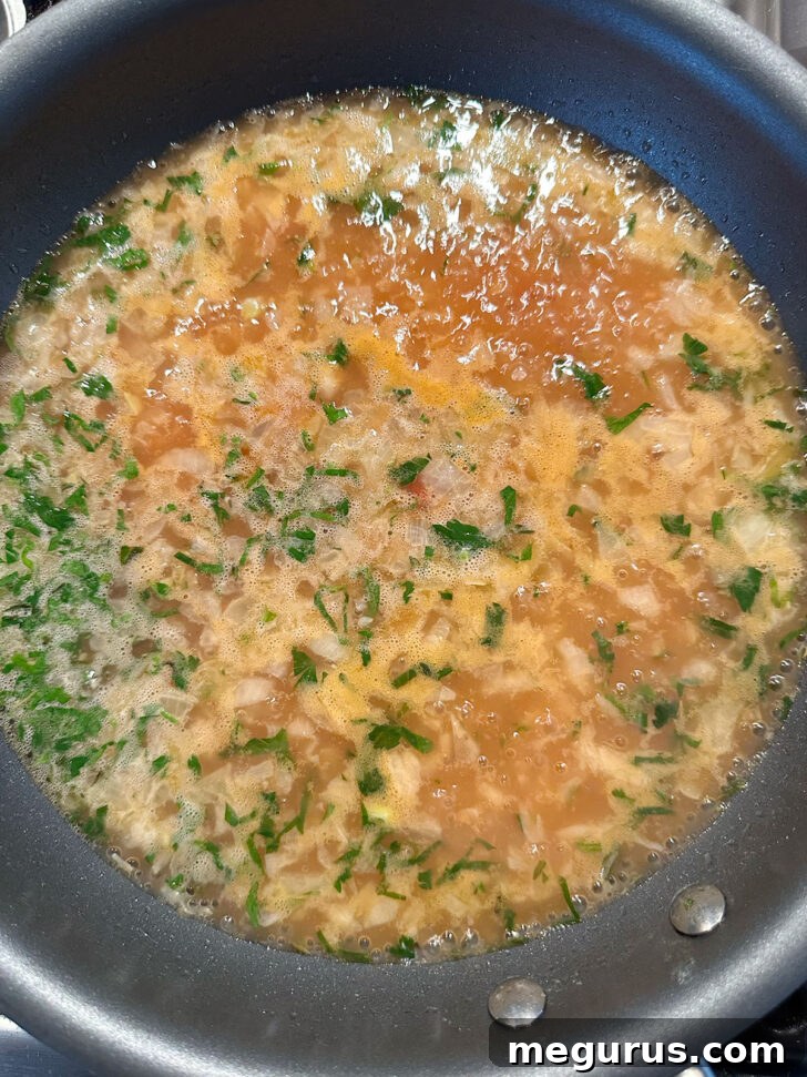 The savory onion and sauce mixture simmering gently in a skillet, reducing to a thicker consistency.