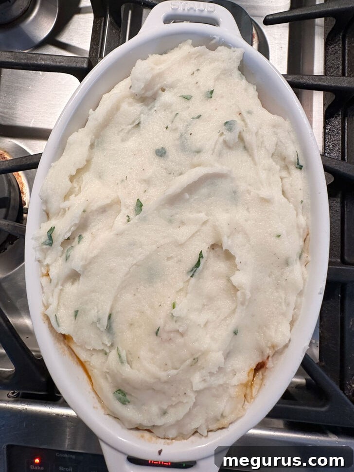 A generous layer of creamy mashed potatoes carefully spread over the corned beef filling in the baking dish.