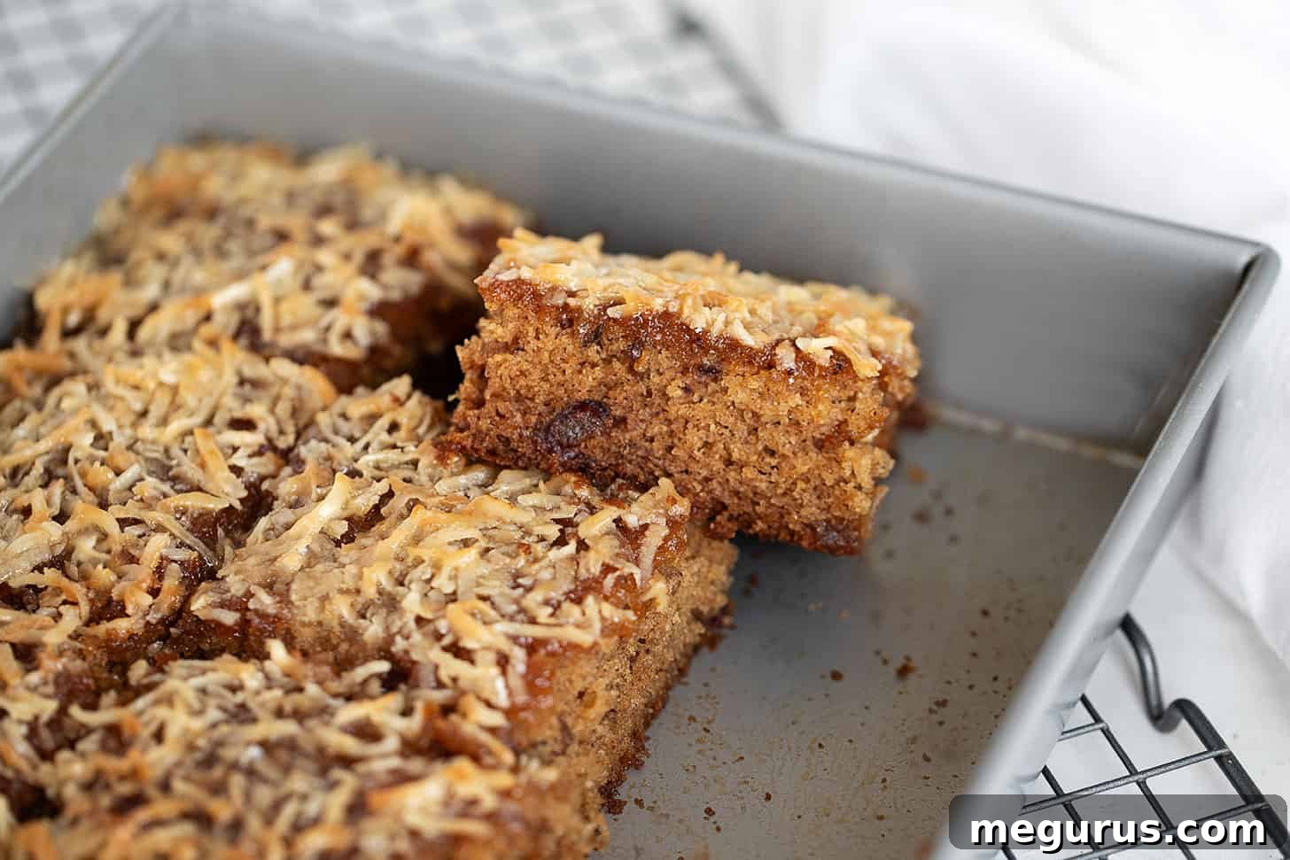 Sliced Queen Elizabeth Cake in a baking pan, showing the moist date cake and golden coconut topping